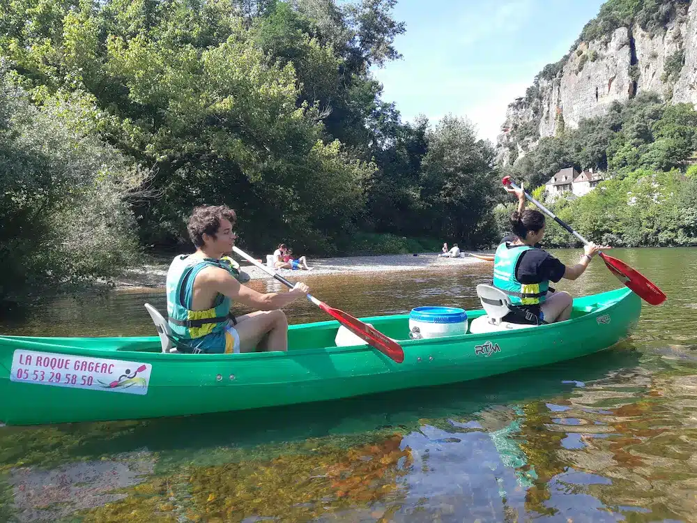 Deux personnes en canoë naviguant sur la Dordogne près de La Roque-Gageac, avec falaises et végétation en arrière-plan.